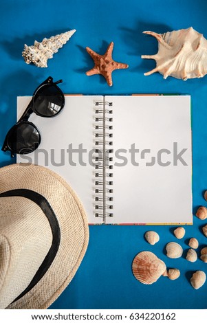 Bright blue picture with an open notebook, small and large shells, light hat and sunglasses with copy space