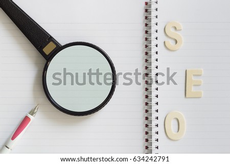 Wood Letters was Arranged as SEO Abbreviation (Search Engine Optimization) with Pen and Magnifying Glass (Magnifier) on Blank Notebook. Idea Concept for Organization, Business, Technology System.