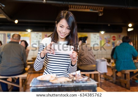 Young Woman taking photo with cellphone on seafood barbecue