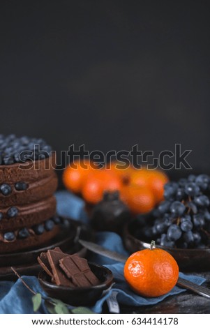 beautiful chocolate cake, decorated with fruit blueberries in a brown ceramic bowl on kitchen towel blue on a black background with a piece of gum trees