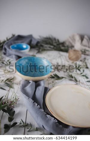blank ceramic plate dinnerware handmade beige blue gray colors for kitchen purple towel white wooden background decorated with greenery, baby's breath eucalyptus close-up top view