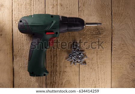 Cordless screwdriver with screws on wooden floor. Close-up