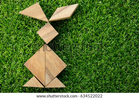 Wooden tangram puzzle in rabbit shape on artificial green grass background (Concept of Happy Easter)
