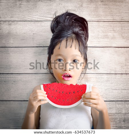 Little asian girl eat watermelon on wood plank background