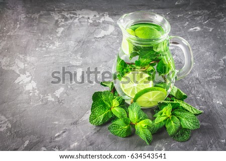 Mojito with mint and lime in a glass and a jug with tubes. Grey marble background