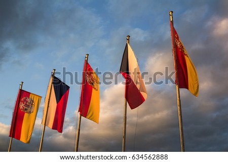 National flag of Czech Republic and Flag with coat of arms of City of Prague. Sky with dark stormy clouds in the background. Yellow evening light