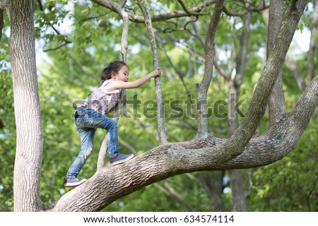 Happy Little Girl climbing a tree Royalty-Free Stock Photo #634574114