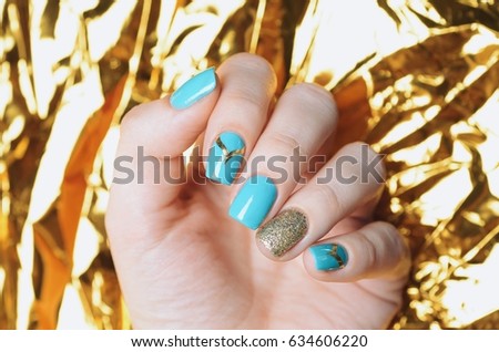 Mint blue manicure with gold glitter on the gold foil background