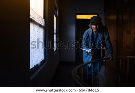 Portrait of asian man standing near window in vintage room, reading book and relaxing, dramatic scene.
