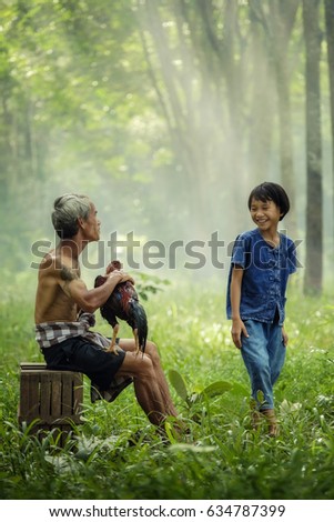 Smiling old parent and his child are very happy, they are happy family in leisure time. father and children daughter having fun and playing in nature. Father hold thai gamecock near daugther standing