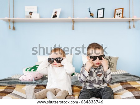 Portrait of brother and sister in sunglasses sitting on bed at home.