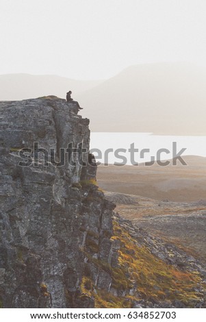 Hiker on a rocky cliff during the sunset. Great atmosphere with light and a spectacular perspective. Tough nature in Iceland.