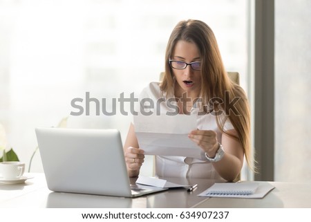 Surprised young businesswoman reading letter at the desk in front of laptop. Woman feels shocked after receiving unexpected news in written message. Female entrepreneur holds notice about loan debt Royalty-Free Stock Photo #634907237