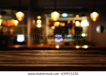 Image of wooden table in front of abstract blurred restaurant lights background. Royalty-Free Stock Photo #634911236