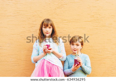 Outdoor portrait of two funny fashion kids, holding drinks, wearing blue and pink clothes