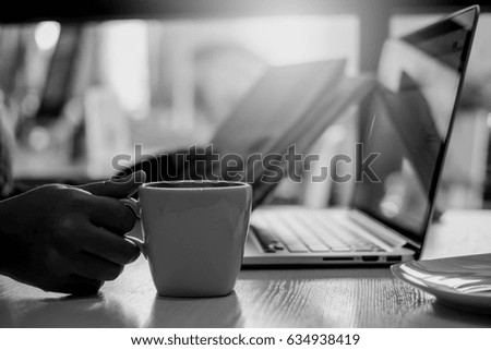 Black and white image of a business woman reading newspaper , holding and drinking coffee in the morning in office