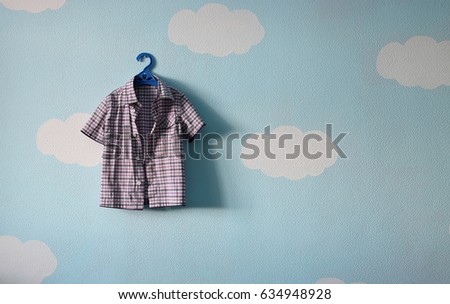 children's shirt hanging on a hanger against the beautiful blue wallpaper 