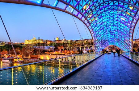 View over the modern glass Peace bridge to the President Palace and Trinity Cathedral on late evening, Tbilisi, Georgia Royalty-Free Stock Photo #634969187