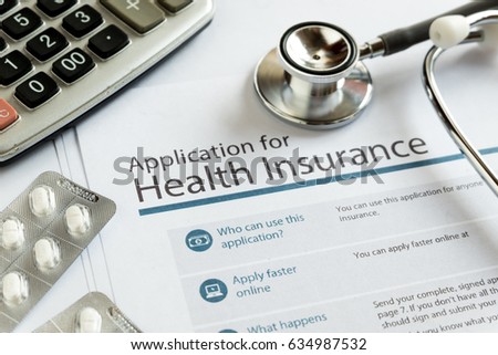 Application for health insurance paper form is overlapped by calculator and stethoscope.