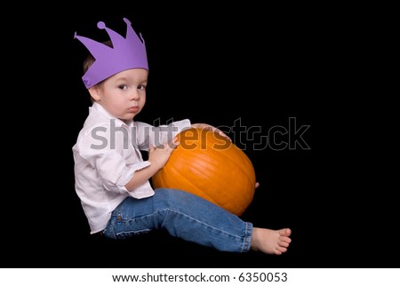 Young boy sitting with a pumpkin and a purple crown isolated over a black background