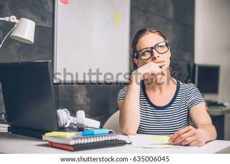 Woman wearing eyeglasses writing notes and contemplating at the office