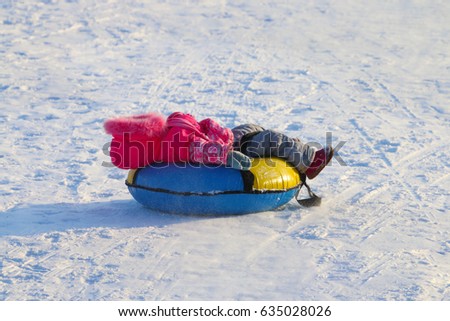 Little girl lies on snowtube down from hill at sunny winter day
