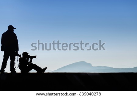 Silhouette of male photographer or traveler taking a photograph sunrise landscape on mountain top, blue tone