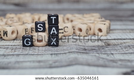 Black plastic block with a GST tax word on blur wooden cube background - Business concept  