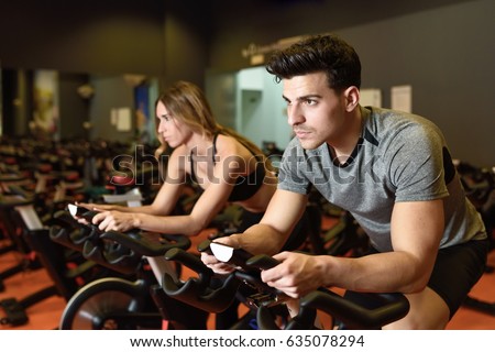 Attractive woman and man biking in the gym, exercising legs doing cardio workout cycling bikes. Couple in a spinning class wearing sportswear. Royalty-Free Stock Photo #635078294
