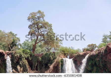 Beautiful photo of Ouzoud waterfall in Morocco with soft flowing water and large colored rocks. Green wild jungles on background