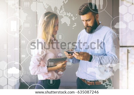 People standing in an office and talking. Man showing woman images on phone.Girl holding tablet computer.In foreground are virtual icons with clouds,people,gadgets. Social media.Man blogging,chatting.