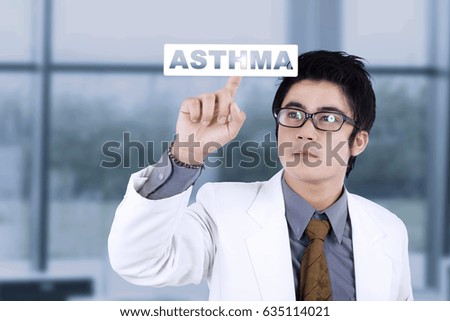 Picture of male doctor touching a word of asthma on the virtual screen while standing in the hospital