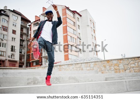 Portrait of jumping stylish african american man on sportswear, cap and glasses. Black men emotion model street fashion.