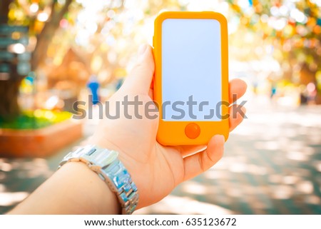 Girl using smart phone at the outdoor park. hand holding smart phone with blank and white screen. Colorful smart phone with vintage tone. hand holding using mobile phone in the public place.