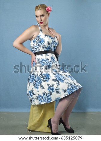 Retro looking blonde woman wearing a blue pattern floral dress. Studio shot and isolated on a blue background