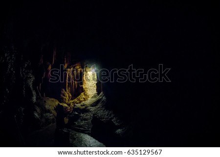 Entrance to the karst cave in a mountain. Natural cave opening. Inside the karst cave background with copy space. Dark cave with a bright daylight spot of exit.