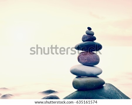 Stacked rounded stones at sea. Small polished pebbles stack on dark wet rock,  blue smooth water of ocean in background