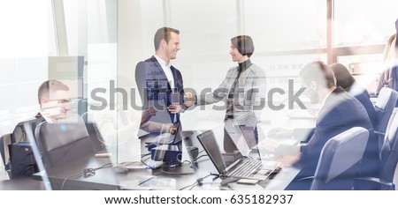 Sealing a deal. Business people shaking hands, finishing up meeting in corporate office. Businessmen working on laptop seen in glass reflection. Business and entrepreneurship concept. Royalty-Free Stock Photo #635182937