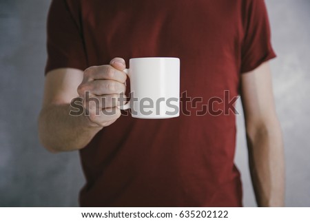 Man in red t-shirt holding big white coffee cup.Mock up of clean coffee cup.Horizontal mockup. Royalty-Free Stock Photo #635202122