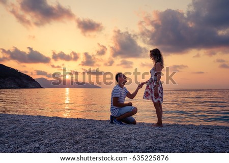 Romantic marriage proposal on the beach at the seaside at sunset over the sea. Young couple in love