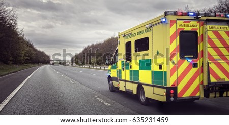 British ambulance responding to an emergency in hazardous bad weather driving conditions on a UK motorway Royalty-Free Stock Photo #635231459