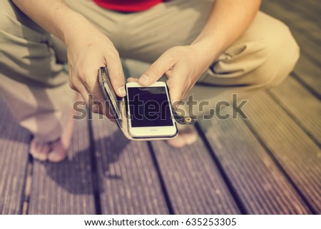 Closeup on man using mobile smartphone over wooden floor background. Photography concept for online connection, communication messaging, banking..