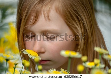 portrait of a little girl of seven years, sniffing daisy flowers in a botanical garden, eyes closed and eyelids lowered, looking at plants, long blond, wheaten hair