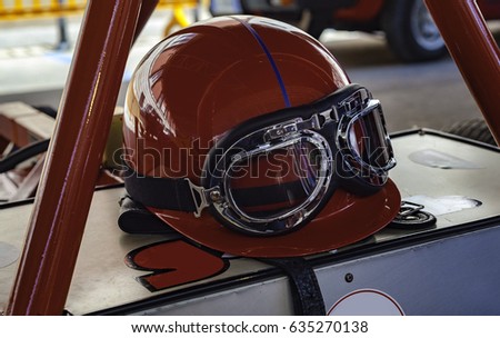 Vintage racing helmet and glasses resting on an antique sports car.
