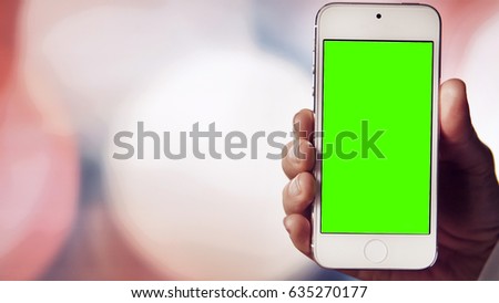 Woman's hand holds white smartphone before bokeh light coloured background