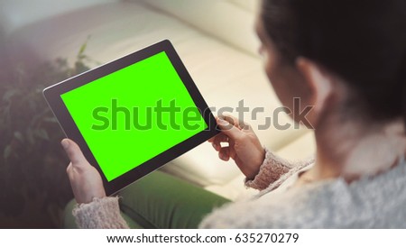 Indoor shot of a woman using tablet pc with green screen sitting on white sofa, horizontal orientation