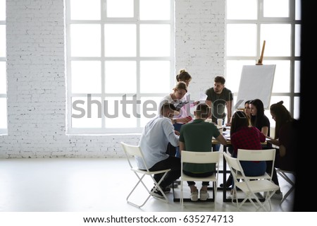 Young classmates writing testing quality control sitting at desk in modern loft interior office, male and female coworkers collaborating on creation startup discussing ideas with professional coach Royalty-Free Stock Photo #635274713