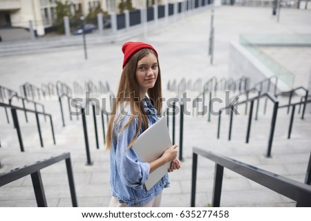 Portrait of female blogger hipster girl walking on the street in urban setting with modern net-book. Beautiful female in trendy outfit holding digital laptop computer and looking at camera