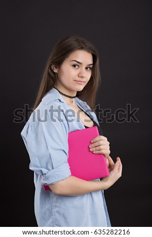 Very Beautiful caucasian girl in denim shirt with long hair, on black background, holds in hands a large crimson color book