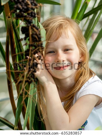 livistona chinensis, portrait, little girl seven years, sitting next palm tree, botanical garden, looking at camera, sweet, smiling, long wheat hair, happy child, sunny, bright , tilt head plant